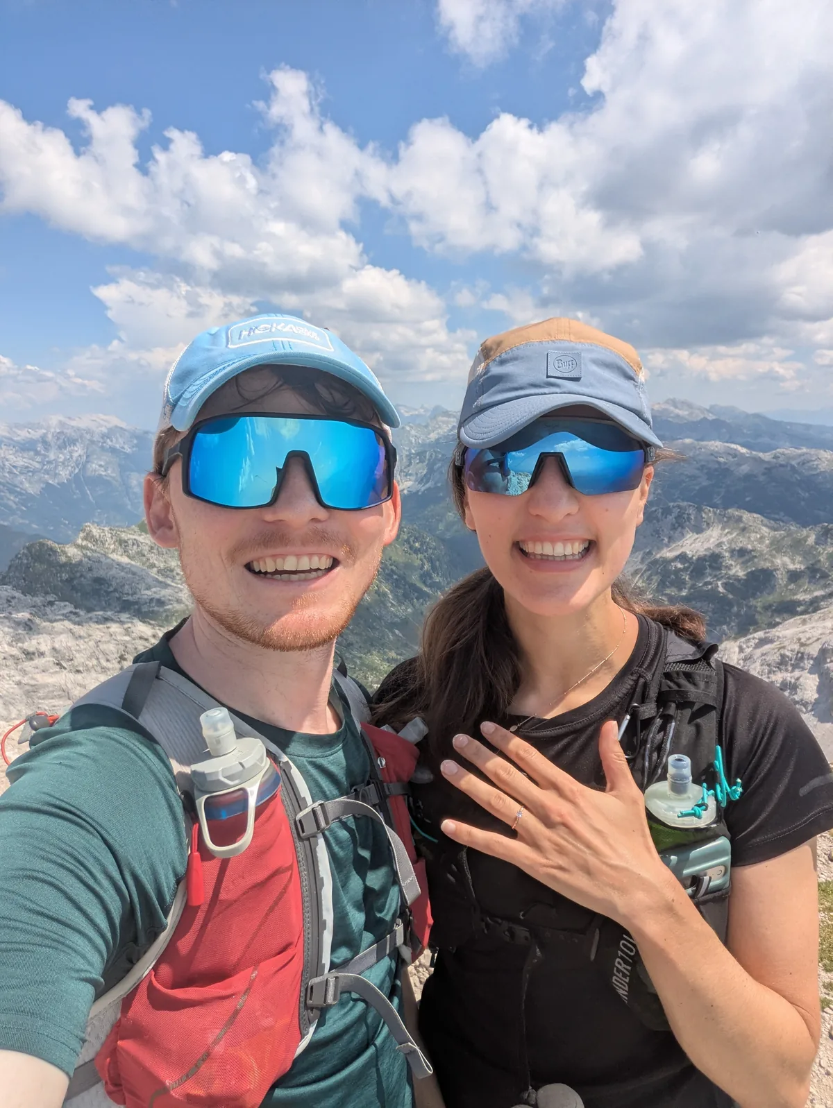 Hannah and Angus on a rocky summit in running vests, Hannah holding up her hand to show the engagement ring.